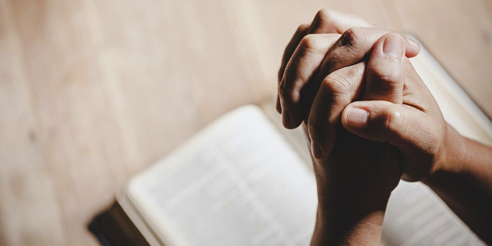 mans hands folded praying over a bible