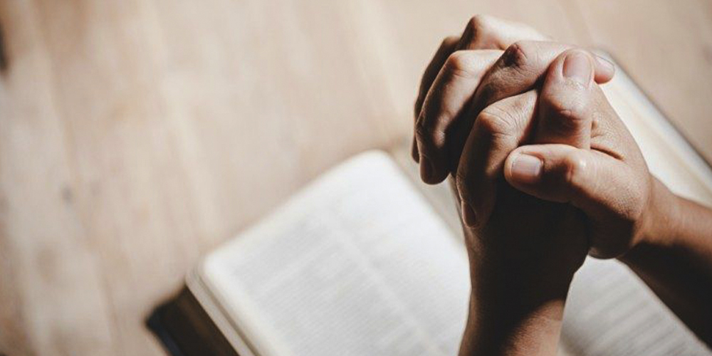hands in prayer over bible