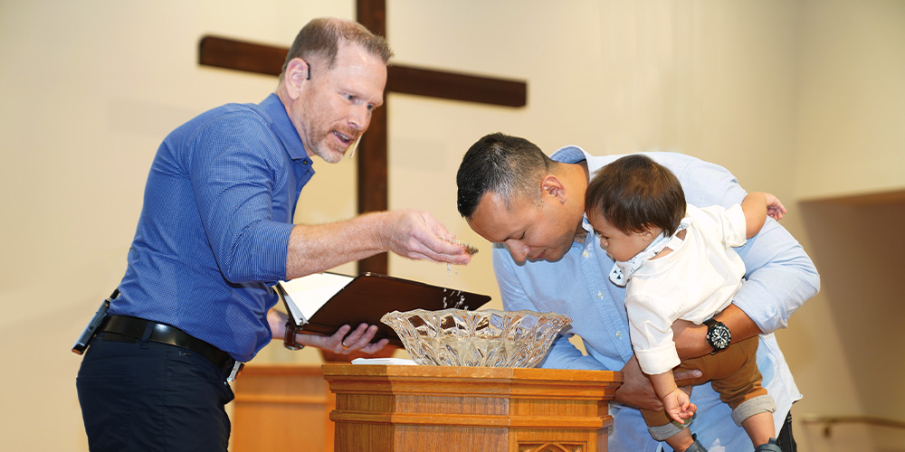 pastor baptizing grown man who is holding his child
