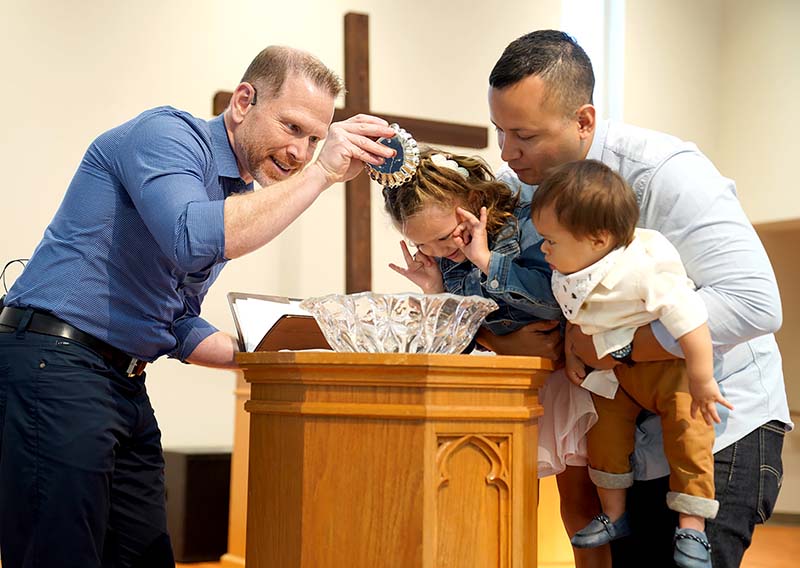Pastor Joel Schulz baptizing young girl being held by father