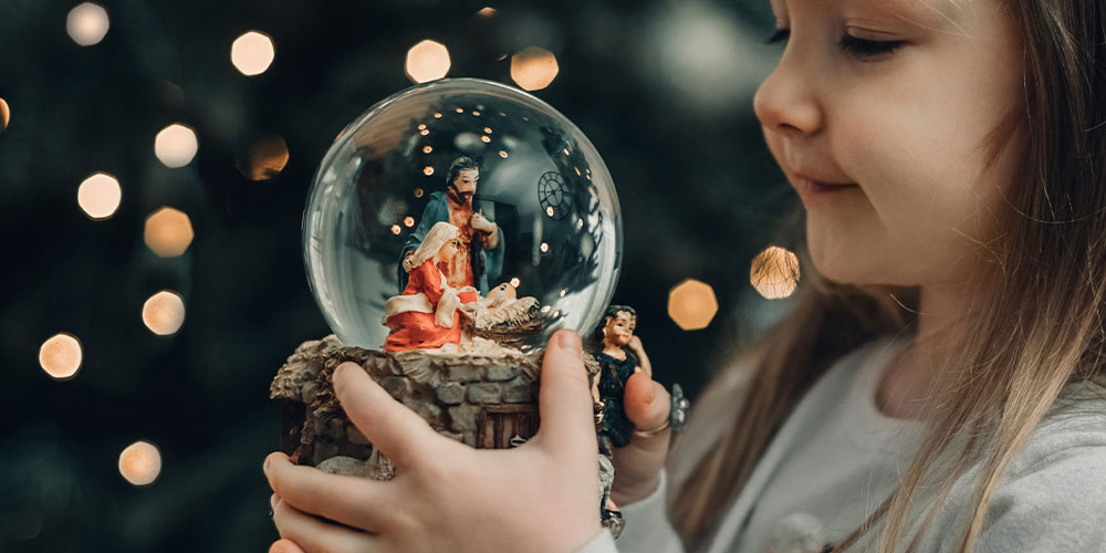 small girls holding a snow globe with Joseph, Mary and baby Jesus inside