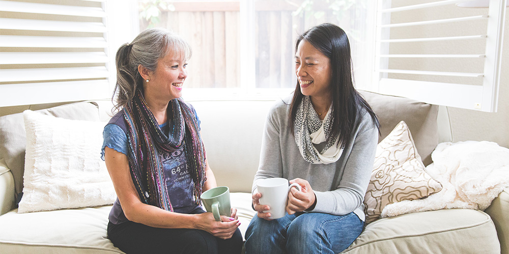 two women talking sitting on couch drinking tea