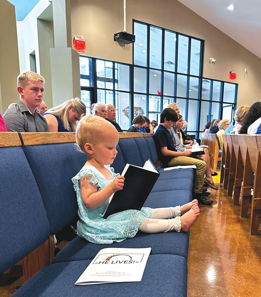 little girl trying to read book in church pew