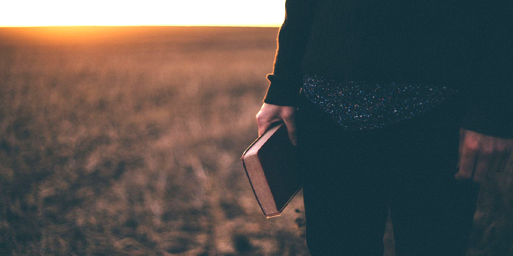 Man walking in field during sunset with bible