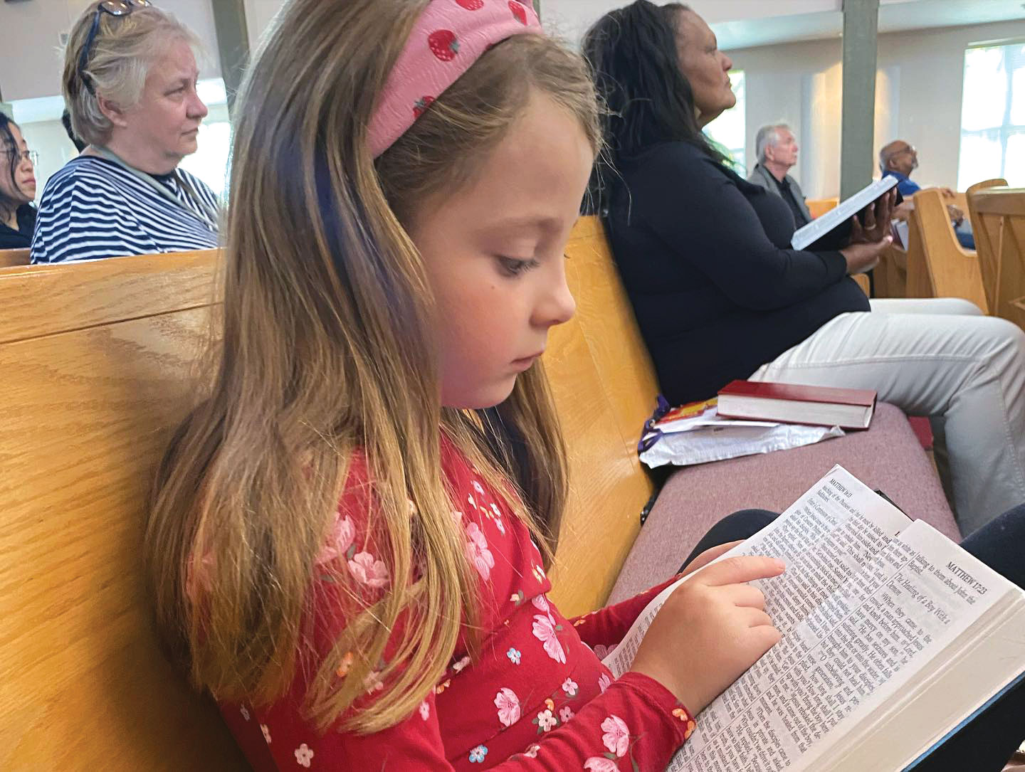 Little girl in church pew reading