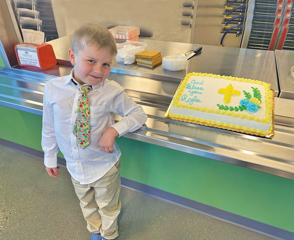 boy with tie standing next to a cake