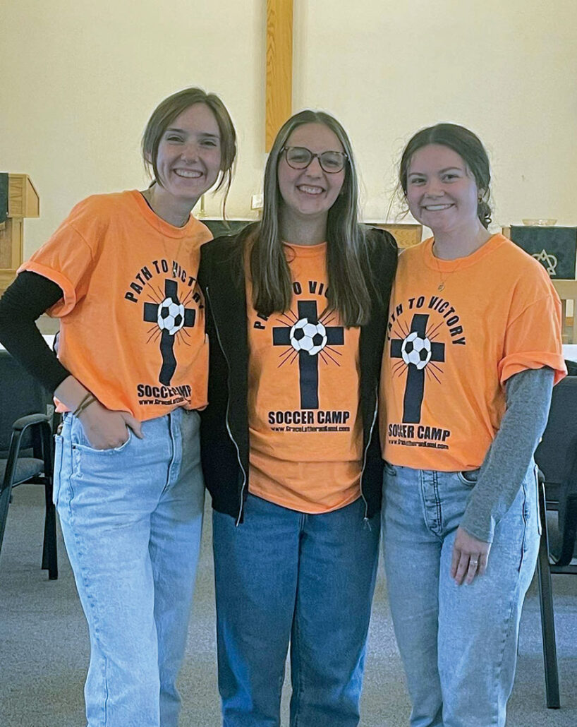 3 teen girls wearing orange soccer camp shirts