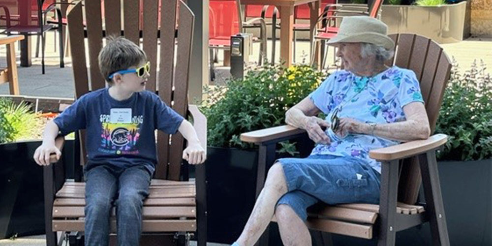 elderly woman and young man sitting on chairs outside talking