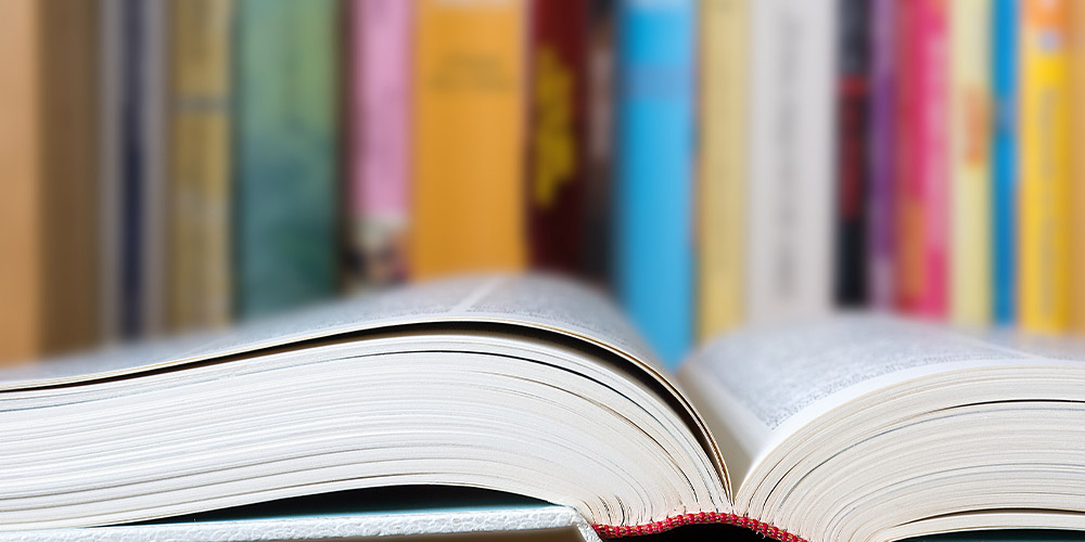 open book in forefront books standing in background with colorful spines. iStock