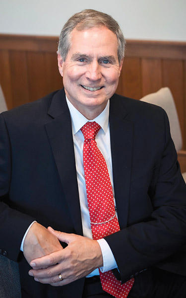 James Pop sitting wearing a black vest with a red tie