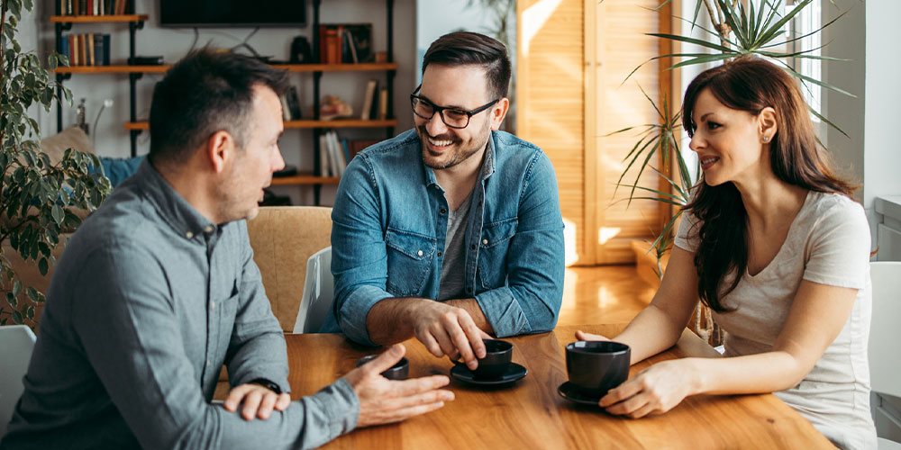two males and female talking over coffee
