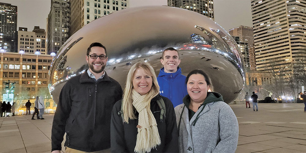 people posing in front of the bean in chicago