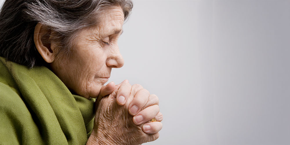 older woman head bow, praying wearing a green scarf