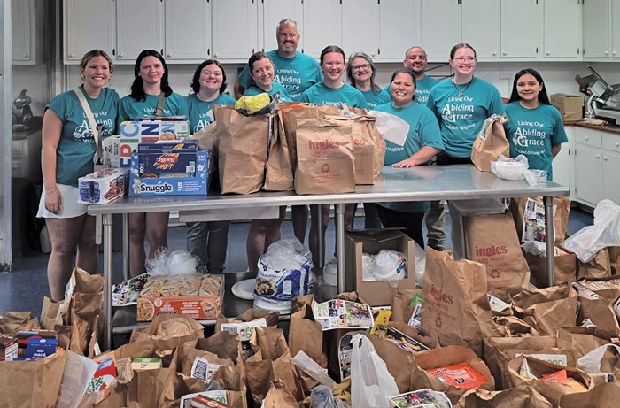 people in a kitchen wearing teal shirts and grocery bags filled with food.