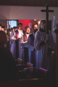 pastors walking up aisle with cross and singing with lit candles