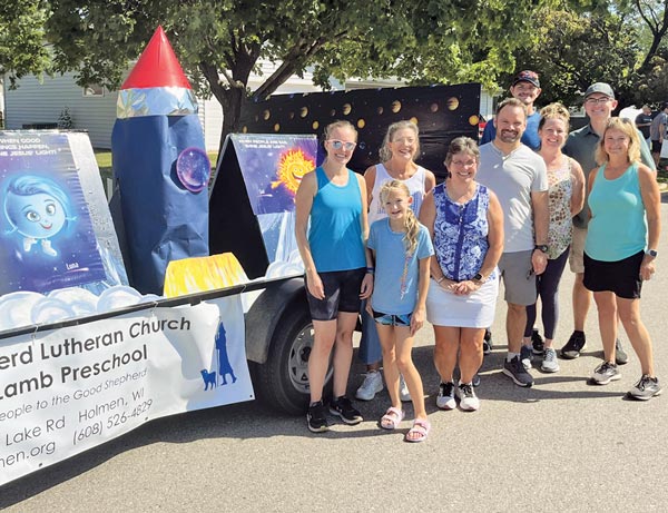 group of people standing in front of parade float. rocket. teal tank