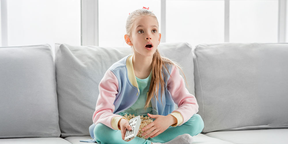 young teen girl on grey couch with remote in hand shocked