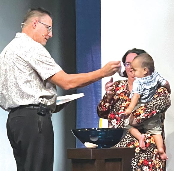 pastor baptizing baby with mom hold him