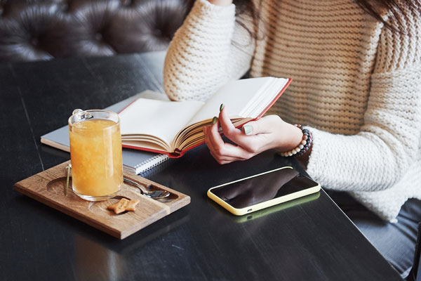 woman drinking orange juice and write in journal phone laying on table