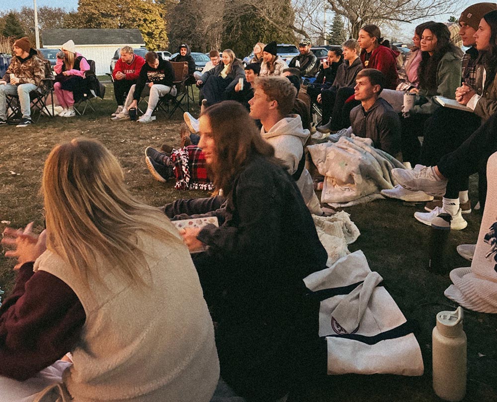 Young people worshiping in a backyard, sitting in camping chairs and on the ground on blankets