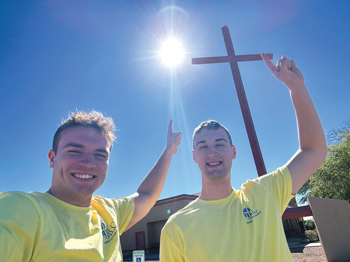 two young adults pointing towards cross and sky