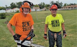 two men cutting down trees wearing safety equipment and send 2 serve shirts