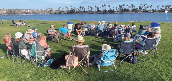 people gathered outside in chairs next to water