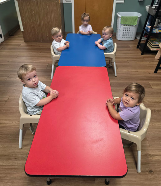 toddlers sitting at table praying with hands folded