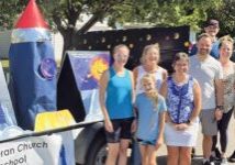 group of people standing in front of parade float. rocket. teal tank